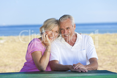 Happy Senior Couple Using Cell Phone at Table By Beach