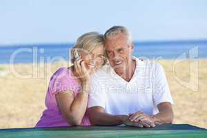 Happy Senior Couple Using Cell Phone at Table By Beach