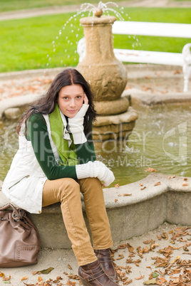 Autumn park young woman sit on fountain