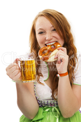 junge rothaarige frau in dirndl hält bier und isst brezel