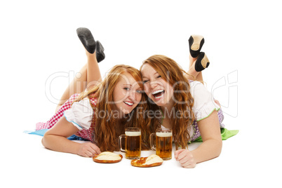 zwei glückliche frauen in dirndl mit bier und brezeln liegen auf dem boden