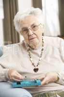 Senior Woman Sorting Medication Using Organiser At Home