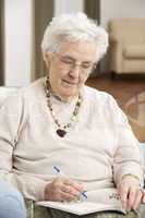 Senior Woman Relaxing In Chair At Home Completing Crossword
