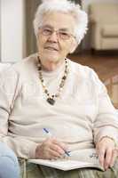 Senior Woman Relaxing In Chair At Home Completing Crossword