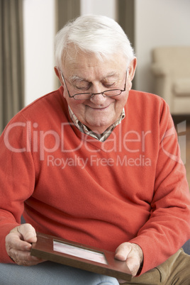 Senior Man Looking At Photograph In Frame