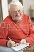 Senior Man Relaxing In Chair At Home Completing Crossword