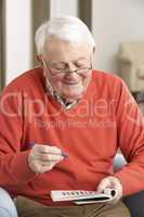 Senior Man Relaxing In Chair At Home Completing Crossword