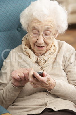 Senior Woman Dialling Number On Mobile Phone Sitting In Chair At