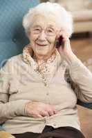 Senior Woman Talking On Mobile Phone Sitting In Chair At Home