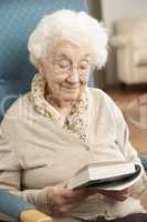 Senior Woman Relaxing In Chair At Home Reading Book