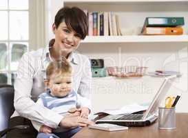 Woman With Baby Working From Home Using Laptop