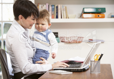 Woman With Baby Working From Home Using Laptop