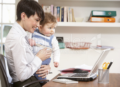 Woman With Baby Working From Home Using Laptop