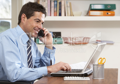 Man Working From Home Using Laptop On Phone