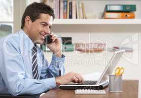 Man Working From Home Using Laptop On Phone