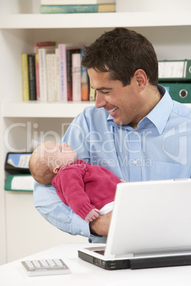 Father With Newborn Baby Working From Home Using Laptop