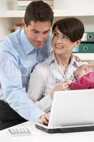 Parents With Newborn Baby Working From Home Using Laptop