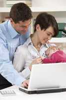 Parents With Newborn Baby Working From Home Using Laptop