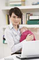 Woman With Newborn Baby Working From Home Using Laptop