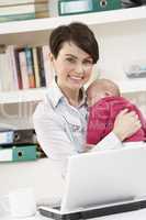 Woman With Newborn Baby Working From Home Using Laptop