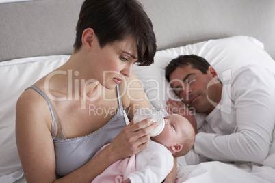Mother Feeding Newborn Baby In Bed At Home