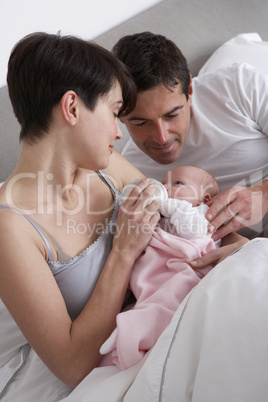 Parents Feeding Newborn Baby In Bed At Home