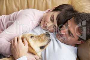 Portrait Of Couple Relaxing On Sofa With Pet Dog At Home