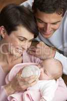 Portrait Of Parents Feeding Newborn Baby At Home