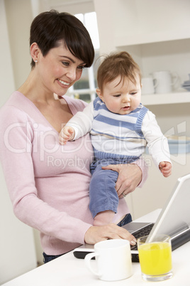 Woman With Baby Working From Home Using Laptop