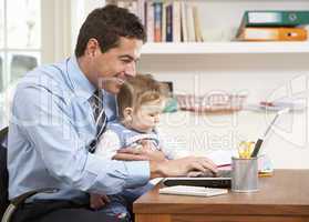 Man With Baby Working From Home Using Laptop