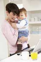 Woman With Baby Working From Home Using Laptop