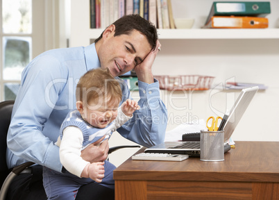 Stressed Man With Baby Working From Home Using Laptop