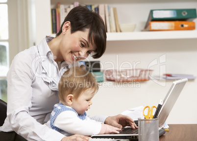 Woman With Baby Working From Home Using Laptop