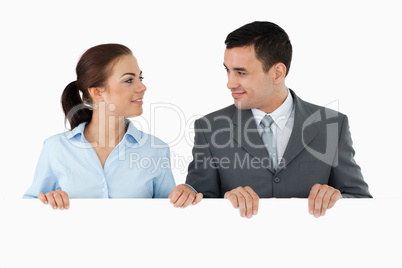 Business partners looking at each other while holding sign toget