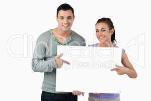 Smiling young couple pointing at sign they are holding
