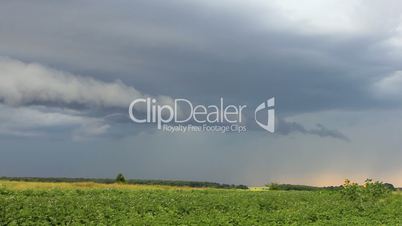 Rain clouds flying on sky over green field time-lapse