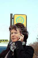 Frau steht an der Bushaltestelle und ruft sich ein Taxi