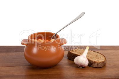 Borsch in clay pot with bread and garlic on wooden table