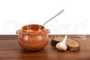 Borsch in clay pot with bread and garlic on wooden table