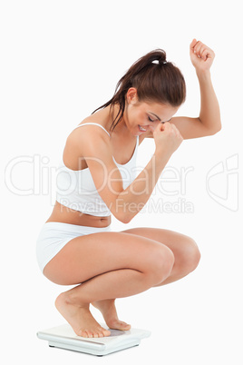Portrait of a happy woman squatting on scales