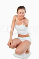 Portrait of a fit woman squatting on scales with the thumb up