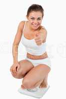 Portrait of a woman squatting on scales with the thumb up