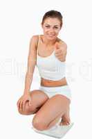 Portrait of a thin woman squatting on scales with the thumb up