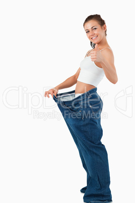 Portrait of a woman wearing too large pants with the thumb up