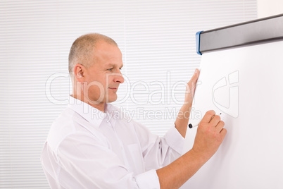 Mature businessman writing at empty flip chart