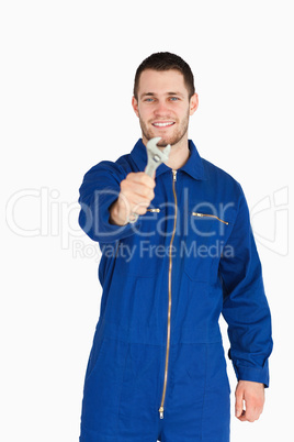 Smiling young mechanic in boiler suit showing a wrench