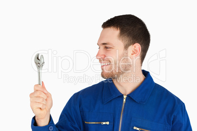 Smiling young mechanic in boiler suit looking at his wrench