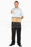 Smiling young post employee with parcel giving thumb up