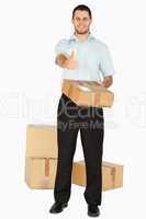 Smiling young post employee with parcels giving thumb up