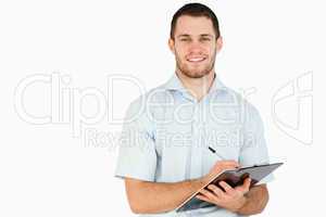 Smiling young post employee taking notes on clipboard
